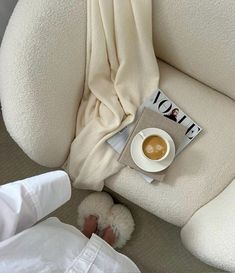 a cup of coffee sitting on top of a white chair next to a person's feet