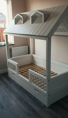 a white bed with a wooden frame and mattress underneath it in a room next to a window