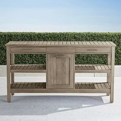 a wooden table with two drawers and one shelf on the top is in front of a hedge