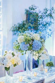 blue and white flowers are in vases on a table with candles around the tables