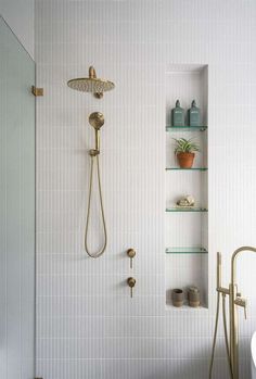 a white bathroom with gold fixtures and shelving on the wall, along with a shower head