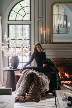 a woman sitting on a chair in front of a fireplace with a blanket over it