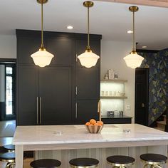 a kitchen island with stools and lights hanging from it's ceiling above it