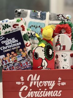 a red box filled with christmas items and books on top of a table next to blankets