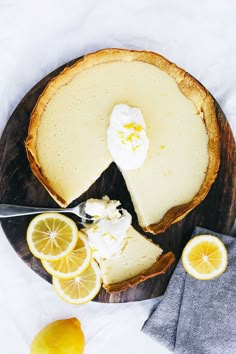 a cheesecake with lemons and whipped cream on a wooden platter next to a knife