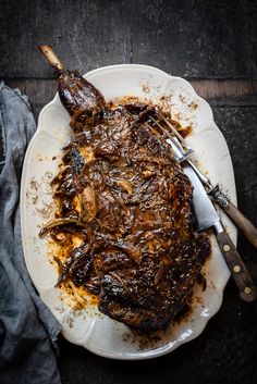 a white plate topped with meat covered in gravy next to utensils