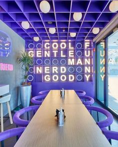 a long table with purple chairs in front of a neon sign that reads cool, gentle man nerdn goody