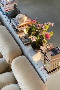 a coffee table topped with books and flowers on top of a white couch next to a window