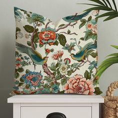 a white pillow with colorful birds and flowers on it next to a potted plant