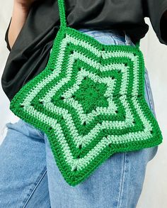 a woman is holding a crocheted green bag in her right hand and wearing jeans