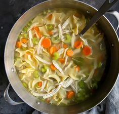 a pot filled with noodles and carrots on top of a table next to a spoon