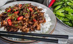 a white plate topped with meat and rice next to chopsticks on a wooden table