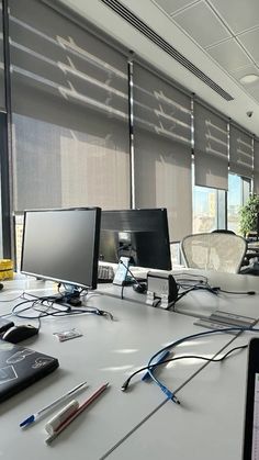 an office desk with two monitors, keyboard and mouse on it in front of the window