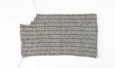 a piece of gray knitted material on a white surface with one stitched at the end