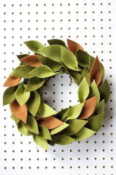 a wreath made out of green leaves sitting on top of a white wall with holes in it