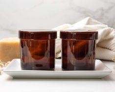 two brown glass jars sitting on top of a white plate next to a soap bar