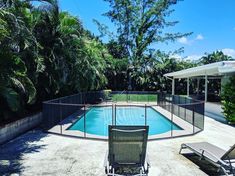 an empty swimming pool surrounded by trees and lawn chairs next to the fenced in area