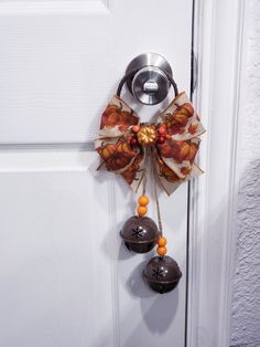 a door handle with two bells hanging from it's side and an orange bow on the front