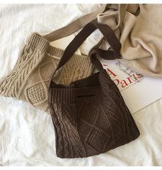 two sweaters and a bag are laying on a white sheet with a book next to them