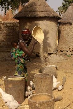 a woman is pouring water into buckets in front of her hut with chickens on the ground