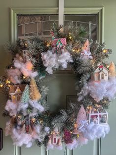 a wreath is hanging on the front door decorated with christmas lights and decorations, including houses