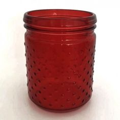 a red glass jar with holes on the bottom and lid is sitting on a white surface