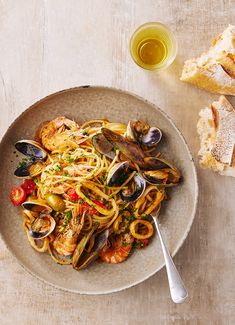 a plate of pasta with clams and mussels next to bread on a table