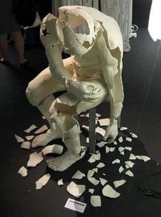 a sculpture of a man sitting on top of a chair covered in pieces of paper