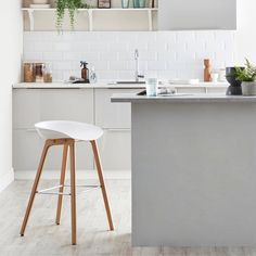 a kitchen with white walls and wooden stools in front of the counter top, next to an island that has plants on it