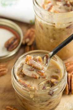 two jars filled with pudding and pecans on top of a wooden table next to a spoon