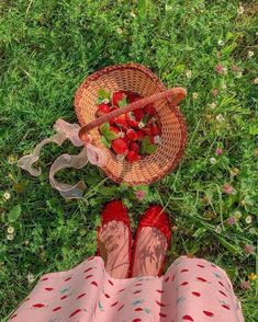 strawberries in a basket on the grass next to a woman's feet wearing red shoes