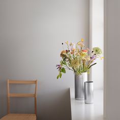 two metal vases with flowers in them on a table next to a wooden chair