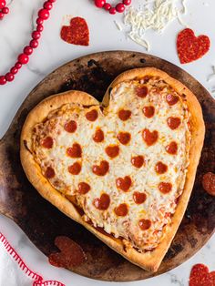 a heart shaped pizza sitting on top of a wooden cutting board