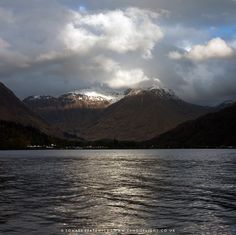 the mountains are covered in snow as clouds loom over them on a cloudy day