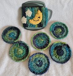 crocheted coasters and pot holders are arranged on a white blanket with a green mug