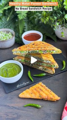 a sandwich cut in half on top of a black plate next to bowls of sauce