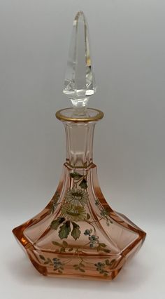 a glass bottle with a gold top and floral designs on it's side, sitting on a white surface