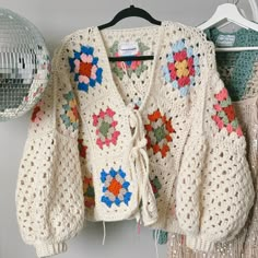 a crocheted sweater hanging on a rack with disco balls in the back ground