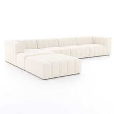 a white sectional couch sitting on top of a white floor next to an ottoman chair