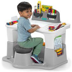 a little boy sitting at a desk with lots of pens and pencils on it