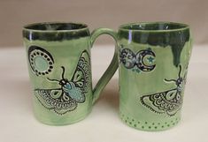 two green coffee mugs with designs on them