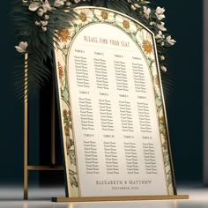 a wedding seating sign with flowers and greenery on it in front of a black background