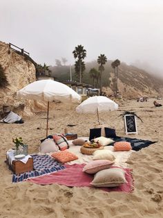 a blanket and pillows on the beach with an umbrella in the sand next to it