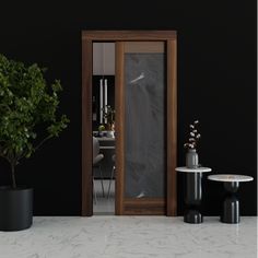 a room with black walls and white marble flooring, two potted plants on either side of the door