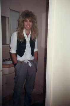 a man with long hair standing in front of a door wearing a white shirt and black vest