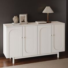 a white cabinet with two doors and a lamp next to it on top of a hard wood floor