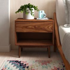 a wooden nightstand with two plants on it next to a white bed and a rug