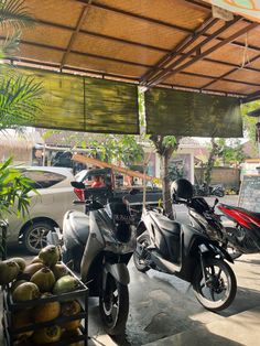 two motorcycles parked under a covered area next to some trees and other vehicles in the background