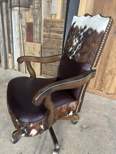 an office chair with cow hide upholstered on the back and arms, sitting in front of a wooden wall