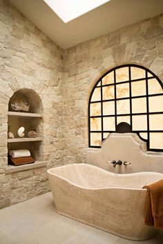 a bathroom with stone walls and an oval window above the bathtub is pictured in this image